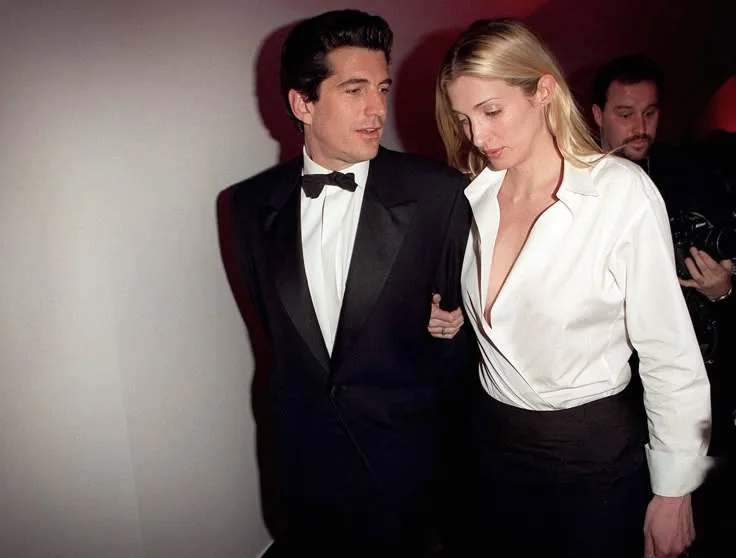 Carolyn Bessette in a low-cut white shirt and black skirt, walking arm-in-arm with JFK Jr. – discreet 90s seduction