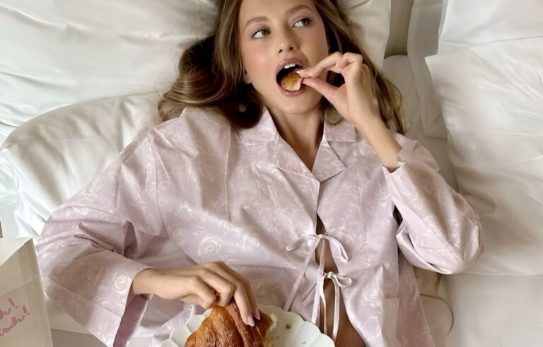 French-inspired morning routine: elegant woman in silk pajamas enjoying a croissant in bed