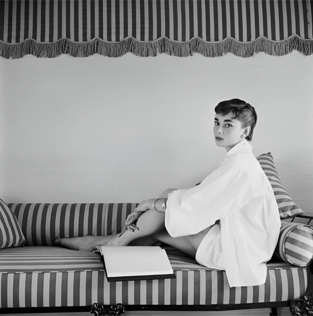 Audrey Hepburn sitting gracefully on a sofa, representing elegant feminine presence in timeless fashion.