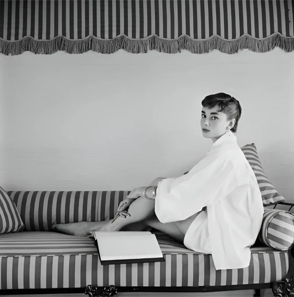 Audrey Hepburn sitting gracefully on a sofa, representing elegant feminine presence in timeless fashion.